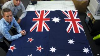 Flagmakers Victor Gizzi (L) and David Moginie pose next to flags of New Zealand (L) and Australia (R) in their factory near Wellington, New Zealand on 3 March 2014