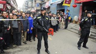 Police stand guard in front of local residents near a crime site on a street in Changsha, Hunan Province, 14 March 2014