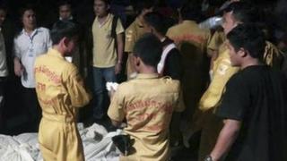In this photo taken Monday, 24 March 2014, Thai charity workers and onlookers stand next to bodies of victims of a road accident, wrapped in white cloths, foreground, in Mae Sot, northern Thailand