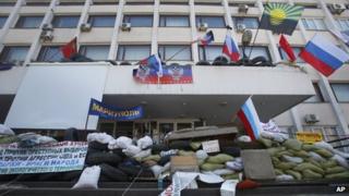 Masked pro-Russian protesters stand behind a barricade in front of the city hall as flags meant to represent the Donetsk Republic fly alongside Russian flags in Mariupol, Ukraine, Thursday, April 17, 2014.