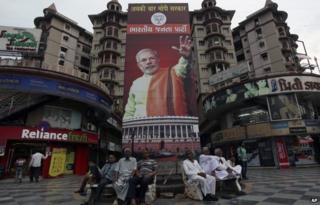 Indians sits on benches in front of a hoarding of India's main opposition Bharatiya Janata Party(BJP) prime minister candidate Narendra Modi at a shopping complex in Ahmadabad.