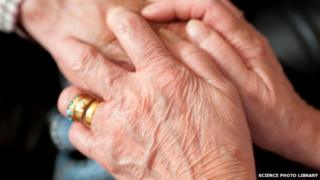 Elderly woman being comforted by a carer who is holding her hands.
