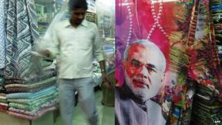 A Indian man walks past a sari, with a portrait of Indian Prime Minister Narendra Modi, displayed outside a shop in New Delhi