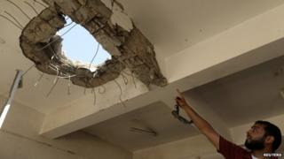 A teacher points to a hole in the ceiling after a building was bombed by a Libyan warplane at a university in Benghazi (1 June 2014)