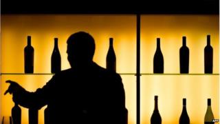 A man in silhouette picks a bottle of cognac