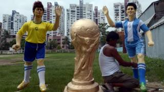 An Indian artist gives finishing touches to a clay idol of Argentine soccer player Lionel Messi (R) alongside a clay idol of Brazilian soccer player Neymar and a replica of FIFA World Cup for a football club, outside the workshop in Kolkata on June 10, 2014.