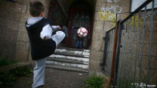 Child kicks ball at run-down building