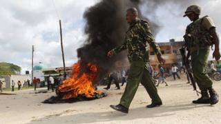 Kenyan police officers walk past a fire used to barricade a main road after unidentified gunmen recently attacked the coastal Kenyan town of Mpeketoni on 17 June 2014