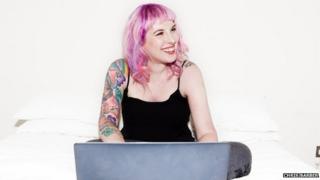 Kat Williams, blogger with pink hair and tattoos sits at her laptop