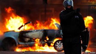 Police officer and burning car during riots of August, 2011