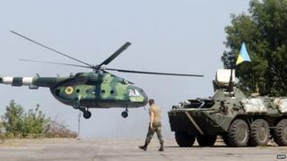 A serviceman walks near an APC while a helicopter flies on the position of the Ukrainian troops in Donetsk region on August 9