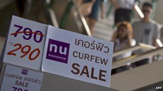 Tourists walk past discount promotion placards displayed at a shop in Bangkok