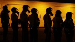 Police wearing gas masks stand by a wall in Ferguson, Missouri