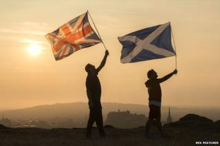 Two men holding flags aloft over Edinburgh - union jack and Saltire