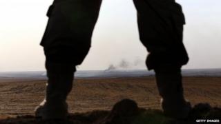 An Iraqi Kurdish Peshmerga fighter holds a position as smoke billows on the front line in Khazer, 40 km West of Irbil, in northern Iraq on 16 September 2014.