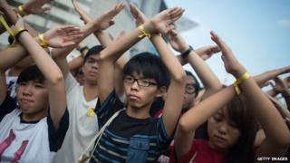 Джошуа Вонг (в центре) делает крест руками на церемонии поднятия флага в Гонконге 1 октября 2014 года
