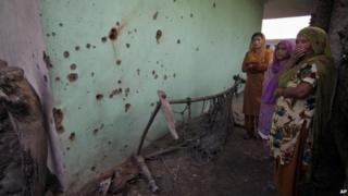 Indian women look at shell marks allegedly caused from firing from Pakistan side at Garkhal village near the India-Pakistan international border, 35 kilometers (22 miles) from Jammu, India, Friday, Oct. 25, 2013