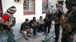 Iraqi security forces and gunmen rest on a sidewalk following clashes with jihadists in Ramadi, the capital of the western province of Anbar, 19 September 2014