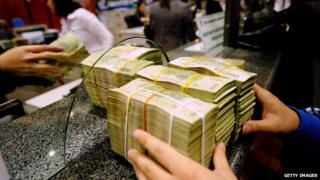 A costumer (R) deposes bricks of dong bank notes to a local commercial bank in Hanoi on February 23, 2011
