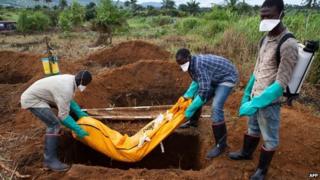 Volunteers in protective suits bury the body of a person who died from Ebola in a village outside Freetown, Sierra Leone - 7 October 2014