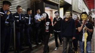 Pro-democracy protesters wearing Guy Fawkes masks walk past policemen on a road occupied by protesters as part of the Occupy Central civil disobedience movement at Mong Kok shopping district 5 November 2014, the day marking Guy Fawkes Night