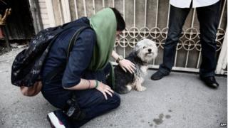 A woman pets her dog on a street in Tehran