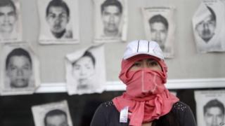 Студент в капюшоне виден перед портретами некоторых из 43 пропавших студентов на платных дорогах на шоссе Чильпансинго-Акапулько 12 ноября 2014 года.
