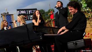 Yanni playing the piano on stage with four vocalists