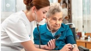 An elderly lady in a wheelchair has her pulse taken by a nurse.