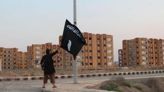 Islamic State fighter waves flag at the base of Division 17 in Raqqa province, Syria