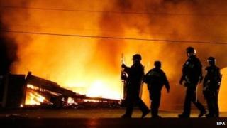 Полиция в защитном снаряжении проходит мимо горящего здания в Фергюсоне, штат Миссури