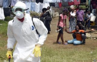 People look on at an Ebola worker in Monrovia, Liberia, on 4 October 2014