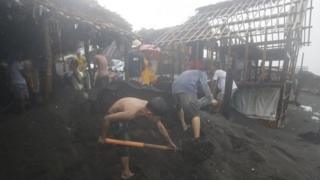 A young boy helps others in shovelling out sand from their homes in Legazpi, Albay province, eastern Philippines Monday, Dec. 8