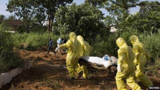 A burial team wearing protective clothing prepare the body of a person suspected to have died of the Ebola virus for interment in Sierra Leone