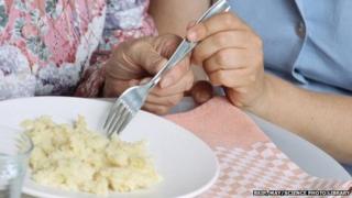 An elderly lady receiving help from a nurse with her meal