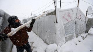 A Syrian refugee uses a pole to try to clear snow from the roof of his tent in Deir Zannoun village, in the Bekaa Valley, east Lebanon (7 January 2015)