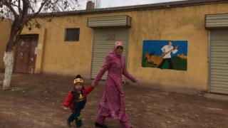 Женщина и ребенок проходят мимо здания с росписью на боку
