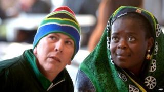 Белый мужчина и черная женщина смотрят поминальную службу Нельсону Манделе по телевизору в баре в Соуэто 10 декабря 2013 года в Южной Африке