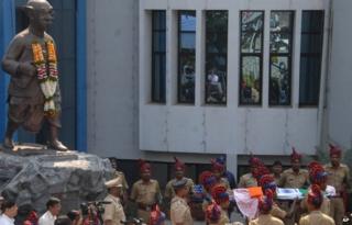 Security officers carry the body of acclaimed Indian cartoonist R. K. Laxman past a statue of the ‘Common Man’, in Pune, India, Tuesday, Jan. 27, 2015.