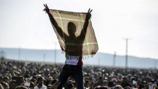 Во вторник курдский народ высвечивает знак V для победы во время праздничного митинга возле турецко-сирийской границы в Суруке, в турецкой провинции Шанлыурфа. Курдские бойцы подняли флаг Народных подразделений защиты на холме, возвышающемся над Кобане в понедельник
