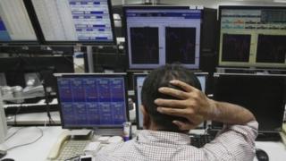 An employee in Tokyo reacts as he works in front of monitors displaying fluctuations of the exchange rates of major currencies