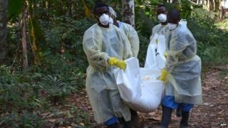 Red cross workers, wearing masks, carry the body of a person who died from Ebola during a burial with relatives of the victims of the virus, in Monrovia, on 5 January 2015.