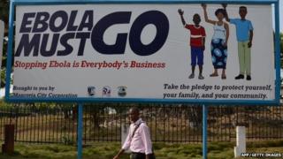 A man walks past an Ebola campaign banner with the new slogan "Ebola Must GO" in West Africa on 23 February 2015.