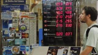 Man walks past board showing currency rates