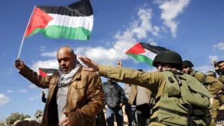 Israeli soldiers with Palestinians carrying their national flag as they protest the confiscation of Palestinian lands by Israel and Jewish settlers near the Jewish settlement Beit Ayin south of the West Bank city Hebron, 07 February 2015