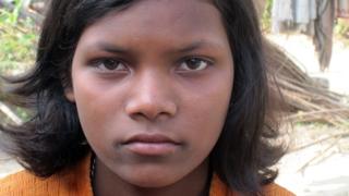 Bijiita Ekka stares fiercely at the camera. She wears an orange shirt and has chin-length hair.