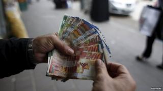 A Palestinian money exchanger holds money at a market in the West Bank city of Ramallah (25 March 2015)