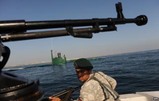 An Iranian Army soldier stands guard on a military speed boat, passing by a submarine during the 'Velayat-90' navy exercises in the Strait of Hormuz in southern Iran on 28 December 2011 as Iran started 10 days of naval drills from 24 December covering east of Strait of Hormuz and the Gulf of Oman to the Gulf of Aden.
