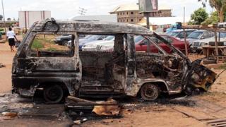 A woman walks near a minibus burnt by an angry mob in reaction to suicide bomb attacks on the Shallom Church of God during church service on Sunday in the Trikania neighbourhood in Kaduna, northern Nigeria political capital 18 June 2012