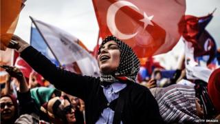 Женщина, поддерживающая премьер-министра Турции Реджепа Тайипа Эрдогана, приветствует и машет флагом Турции и Партии АК (АКП) во время митинга в Стамбуле 23 марта 2014 года
